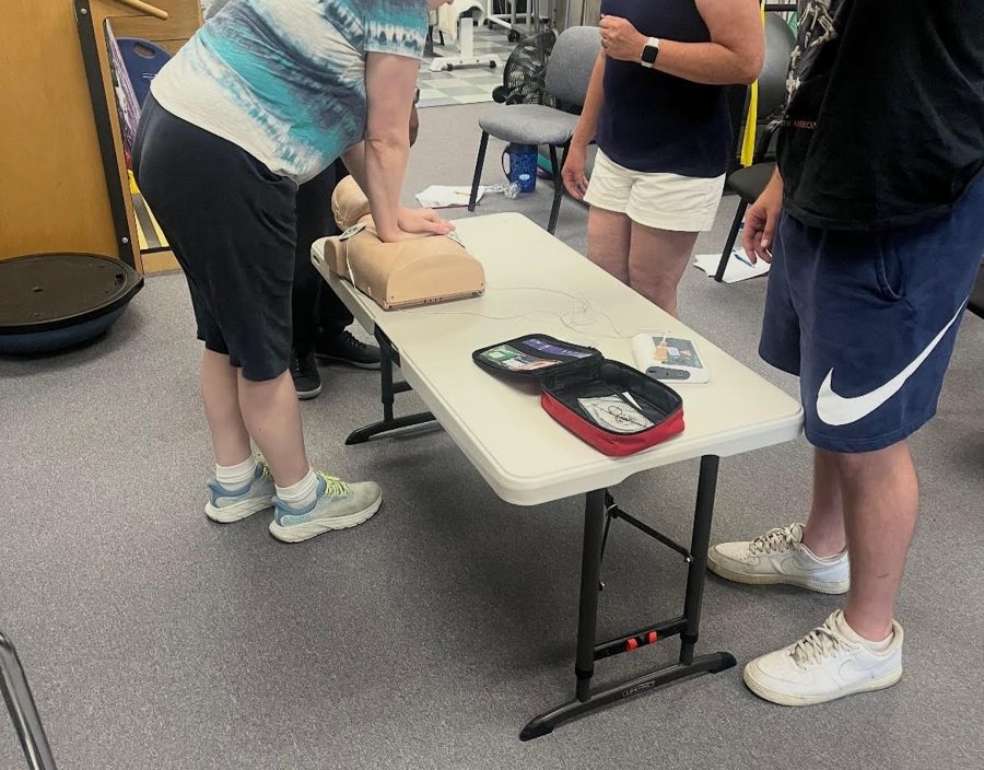 Small group BLS class practicing CPR on a manikin with AED training units