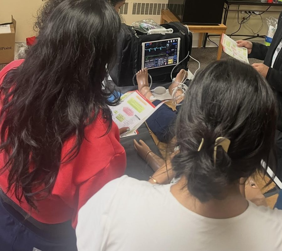 Students reviewing PALS algorithm card next to a pediatric simulator monitor